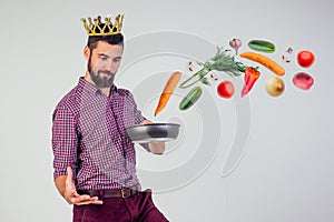 King of the kitchen with a golden crown on head chef holding a frying pan wizard man is cooking magic flying food salad