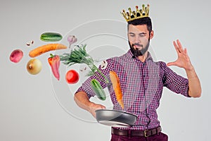 King of the kitchen with a golden crown on head chef holding a frying pan wizard man is cooking magic flying food salad