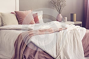 King size bed with pastel pink and white bedding in trendy bedroom interior