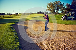 King of the swing. a golfer chipping his ball out of a bunker.