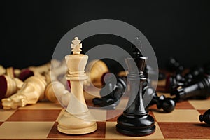 Kings among fallen chess pieces on chessboard against black background, closeup. Competition concept