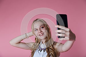 Kinky blonde girl shoots herself smartphone smiling on pink Studio background