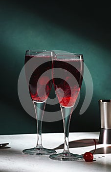 Kir Royale alcoholic cocktail with blackcurrant liqueur, prosecco and cocktail cherry. Dark green background, hard light and