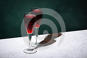 Kir Royale alcoholic cocktail with blackcurrant liqueur, prosecco and cocktail cherry. Dark green background, hard light and
