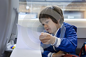 Kisd open a book and reading while traveling to school by the train, Child sitting next to window of a high speed train,