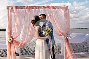 Kiss of the bride and groom, on the pier under the wedding arch