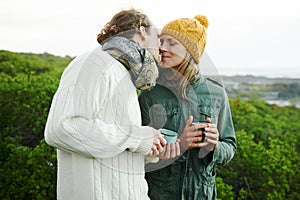 Kiss, couple and drinking coffee in nature on holiday, vacation or travel together on adventure for hiking in winter