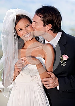 Kiss, happy woman and man at outdoor wedding with smile, love and commitment at garden reception. Romance, face of bride