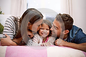 Kiss, parents or kid in bed to smile, lying or relax as happy, hug or bonding together in house. Young family, cheek or