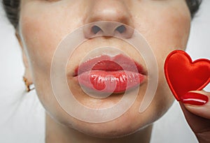 Kiss. Part of a woman face. A small red heart near the woman`s lips.  Red nails