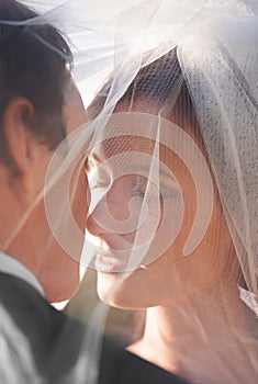 Kiss, veil and couple at wedding with sunshine, love and commitment at outdoor reception. Romance, face of man and woman