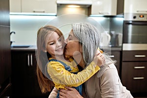 Kisses. Portrait of happy grandmother embracing and kissing her cute little preschool granddaughter, standing together