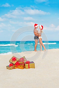 Kissing couple in santa hats at sea beach with christmas golden