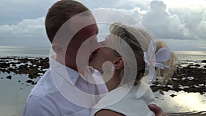 Kissing wedding couple stands against the sunset on a beach in Bali. Close up. Newlywed kiss on a romantic beach. Sweet kiss