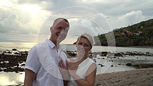 Kissing wedding couple stands against the sunset on a beach in Bali. Close up. Newlywed kiss on a romantic beach. Sweet kiss on Ba