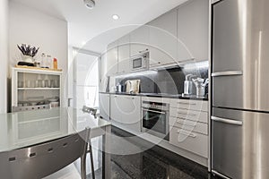 Kitchen of an apartment with glossy black tones of granite on the floor, stainless steel appliances and gray cabinets with metal