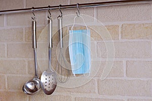Kitchen appliances hang on hooks against a white brick wall, and a medical mask hangs among them.