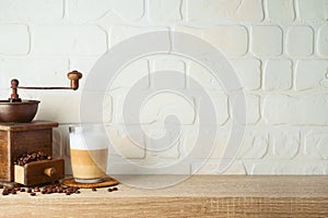 Kitchen background with coffee latte macchiato cup and coffee mill grinder on wooden shelf over brick wall