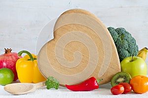 Kitchen board in the shape of heart, vegetables, fruits and spoon. Healthy food concept