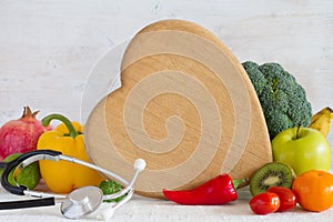 Kitchen board in the shape of heart, vegetables, fruits and stethoscope. Healthy diet food concept