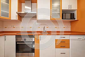 Kitchen with bright orange and white cabinets, drawers and ovens,