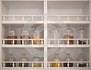 Kitchen cabinet with open shelves, on which there are glass jars with spices, cereals and seasonings