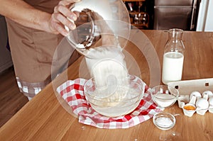 Kitchen. The cook pours the flour from the glass bowl into the dough. Flour. Eggs. Milk