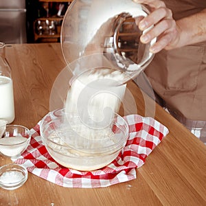 Kitchen. The cook pours the flour from the glass bowl into the dough. Flour. Eggs. Milk