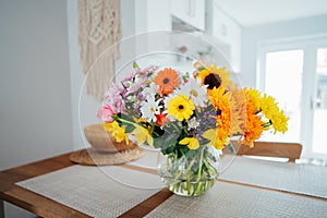 Kitchen counter table with focus on vase with huge multicolor various flower bouquet with blurred background of