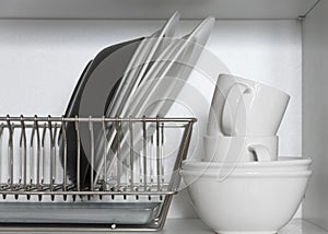 Kitchen cupboard with a lattice for dishes, with a white and black plate, cups, and a drip tray