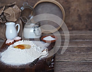 On a kitchen cutting board, a broken egg in flour with ingredients for making dough. Different kitchen utensils