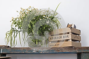 Kitchen decoration. A vase with wild-growing daisies on shabby bench and a box for storing utensils with books