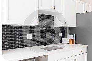 A kitchen detail with white cabinets and black subway tile backsplash.