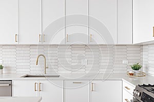 A kitchen detail with white cabinets, gold faucet, and tiled backsplash.
