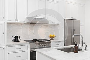 A kitchen detail with white cabinets, stainless steel appliances, and marble countertop.