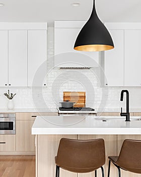 A kitchen detail with white and white oak cabinets and black modern light fixture above the island.