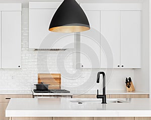 A kitchen detail with white and white oak cabinets and black modern light fixture above the island.