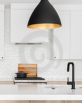 A kitchen detail with white and white oak cabinets and black modern light fixture above the island.
