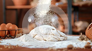 In kitchen of eco bakery, pouring flour on dough for bread, closeup view of organic food on table