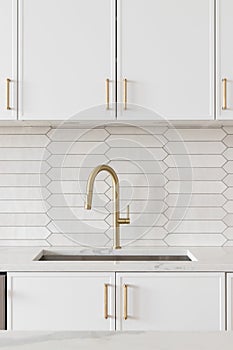 A kitchen faucet detail with a gold faucet, brown backsplash, and white cabinets.