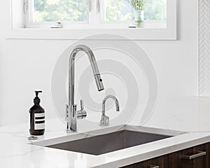 A kitchen faucet detail with a marble countertop and wood cabinet.
