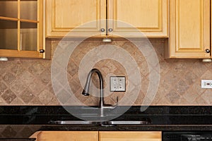 A kitchen faucet detail with wood cabinets and a stone tile backsplash.