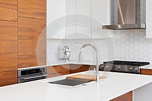 A kitchen faucet detail with wood and white cabinets and a hexagon backsplash.