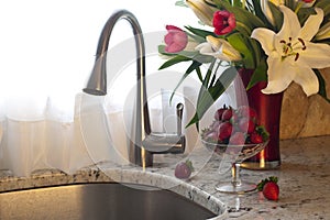 Kitchen faucet, strawberries and fresh flowers on a counter.