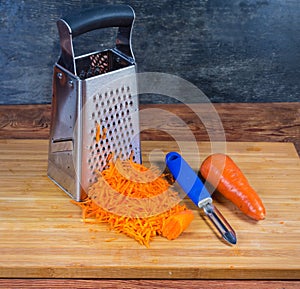 Kitchen grater, grated and uncleaned whole carrots on cutting board