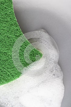 Kitchen green sponge with foam detergent on a gray plate