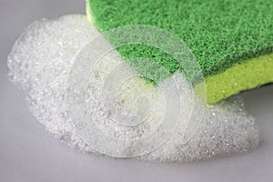 Kitchen green sponge with foam detergent on a gray plate