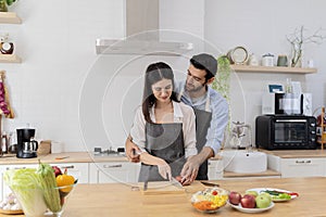 In the kitchen, a happy couple perfectly prepares healthy food, lots of vegetables, a guy juggles with fruits, making her