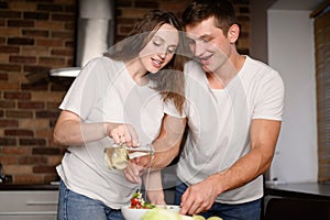 In kitchen, happy married couple prepares healthy food, preparing vegetable salad, dressing with oil, for romantic