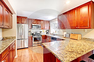 Kitchen with hardwood floor, stained cabinets, stainless steal fridge, and marble counters.